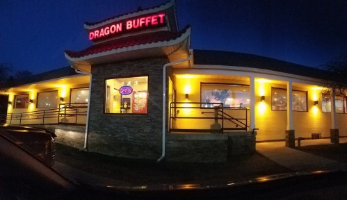 Exterior of Dragon Buffet restaurant at night, illuminated with warm yellow lights and a red "OPEN" sign.