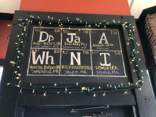 Chalkboard menu displaying beer options and prices, decorated with string lights.