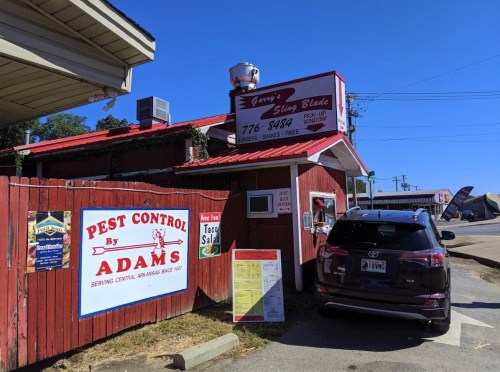 A red building with signs for a restaurant and pest control, featuring a parked car and a clear blue sky.