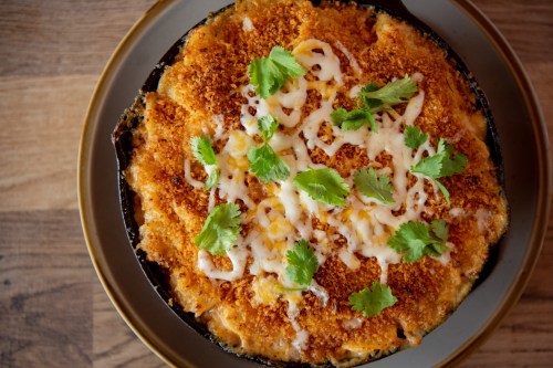 A baked dish topped with golden breadcrumbs, melted cheese, and fresh cilantro on a dark plate.
