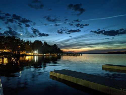 A serene lake at dusk, with colorful clouds reflecting on the water and boats docked along the shore.