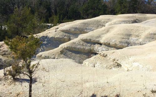A rocky, white landscape with gentle slopes and sparse greenery in the background.
