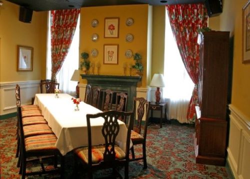 A dining room with a long table, elegant chairs, floral curtains, and a decorative fireplace.