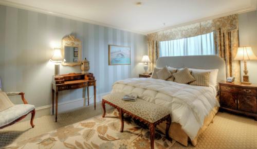 Cozy bedroom with a large bed, elegant decor, soft lighting, and a window with drapes. A chair and table complete the setting.