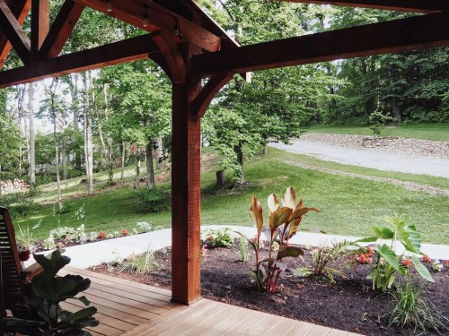 A wooden porch overlooks a lush green garden and a gravel path surrounded by trees.