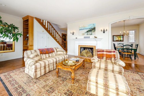 Cozy living room with patterned sofas, a coffee table, fireplace, and dining area in the background. Warm, inviting decor.
