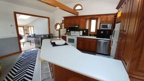 A modern kitchen with wooden cabinets, white countertops, and stainless steel appliances, featuring a cozy seating area.
