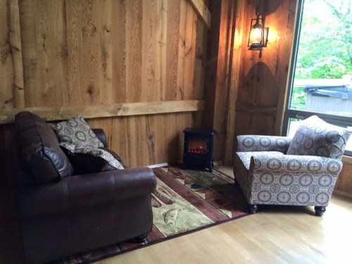 Cozy seating area with a brown leather sofa, patterned chair, and a small electric fireplace in a wooden room.