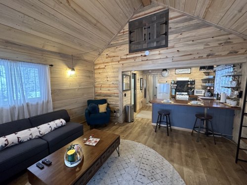 Cozy cabin interior featuring a living area with a sofa, coffee table, and kitchen in a rustic wooden setting.
