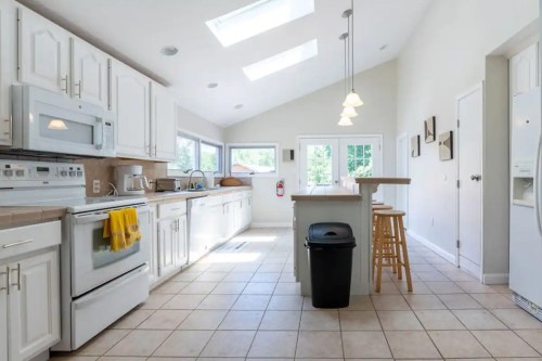 Bright, modern kitchen with white cabinets, skylights, and a central island with a bar stool.