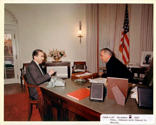 President Johnson and Edward R. Murrow sit at a desk in a formal meeting, with papers and a telephone visible.