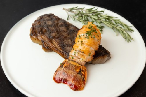 A plate featuring grilled steak and lobster tail, garnished with fresh rosemary.