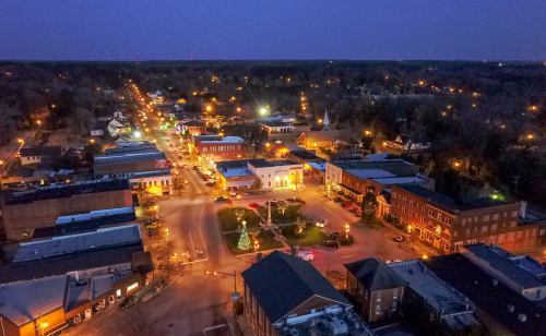 Aerial view of a small town at dusk, with illuminated streets and a central square featuring a Christmas tree.