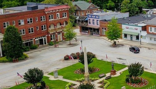 Aerial view of a small town square featuring a monument, greenery, and surrounding buildings.