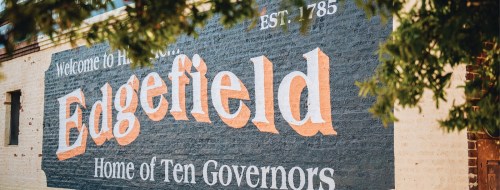 Mural reading "Welcome to Edgefield, Home of Ten Governors," established 1785, on a brick wall surrounded by greenery.