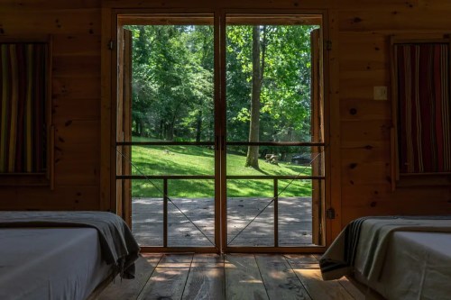 View from a cabin interior, showcasing a wooden door open to a lush green landscape outside.