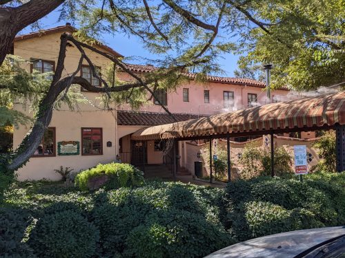 A charming building with a red-striped awning, surrounded by lush greenery and trees on a sunny day.