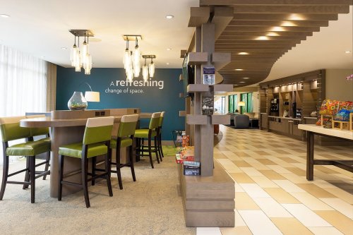 Modern lounge area with a wooden bar, green chairs, and decorative lighting, featuring snacks and a welcoming atmosphere.