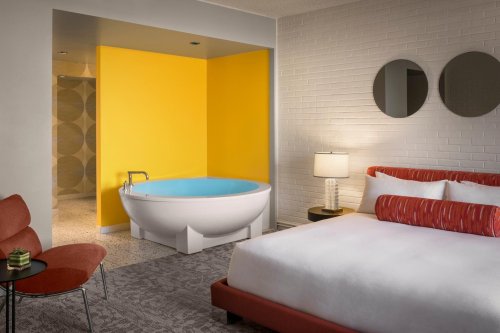 Modern hotel room featuring a bright yellow accent wall, a round bathtub, and stylish furniture.