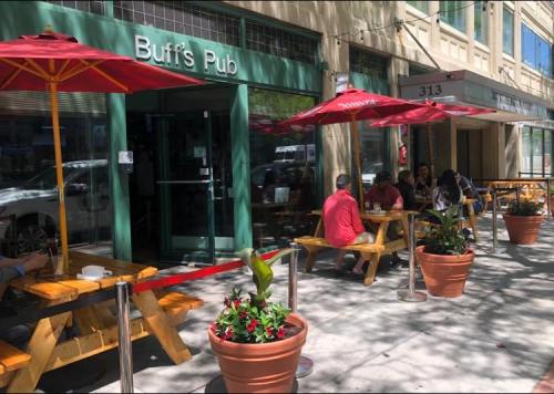 Outdoor seating area of Buff's Pub with umbrellas, patrons at tables, and potted plants along the sidewalk.