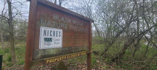 Sign for Black Rock Nature Preserve, indicating it's closed at dusk, surrounded by trees and greenery.