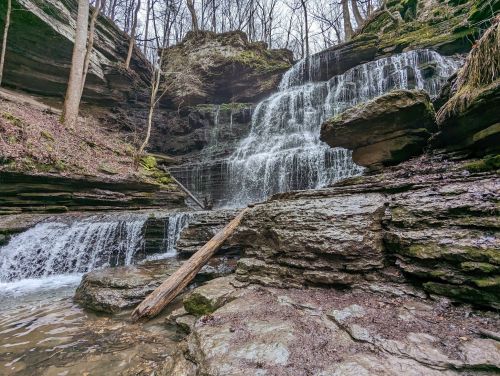 A serene waterfall cascading over rocky cliffs, surrounded by trees and a tranquil pool at the base.