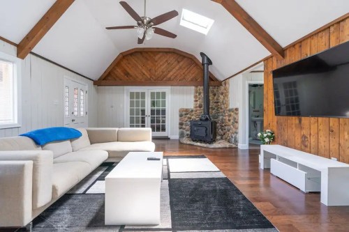 Cozy living room with a stone fireplace, wooden beams, and modern furniture, featuring a large TV and natural light.