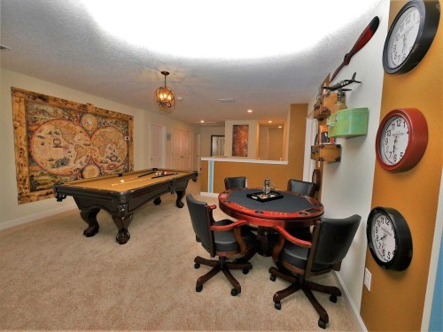 A cozy game room featuring a pool table, poker table, and decorative wall art, with plush seating and clocks.