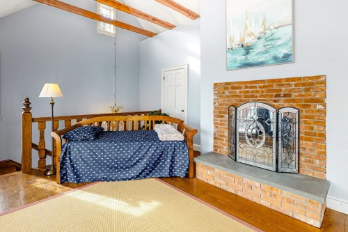 Cozy room with a wooden bench, blue walls, a brick fireplace, and a painting of boats. Warm and inviting atmosphere.
