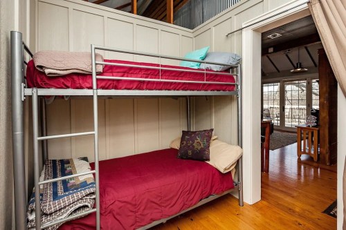 A cozy bedroom featuring a metal bunk bed with red bedding and a view of a bright, open living area.