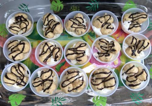 A tray of small dessert cups filled with cookie dough, whipped cream, and drizzled chocolate sauce.