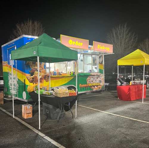 A colorful food truck with "Funnelicious" signage, surrounded by tents in a nighttime parking lot.
