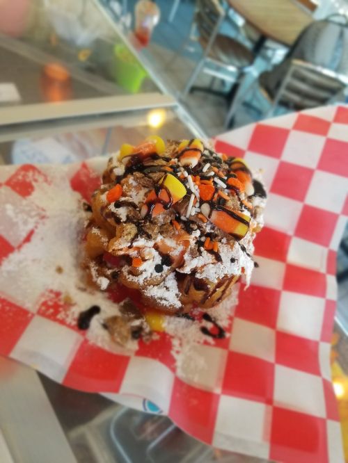 A dessert on a red and white checkered paper, topped with candy corn, chocolate drizzle, and powdered sugar.