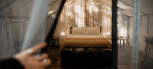 A cozy tent interior featuring a neatly made bed with warm lighting and soft textures, creating a serene atmosphere.