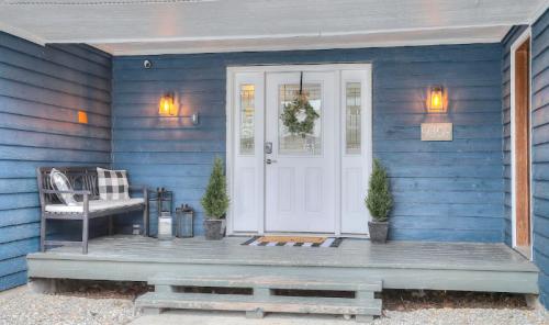 Front porch of a blue house featuring a white door, bench, potted plants, and decorative lighting.