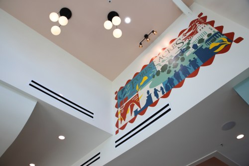 Colorful mural on a wall, depicting a scenic landscape and silhouettes, with modern light fixtures above.
