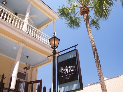 A restaurant sign hangs from a lamp post, with a palm tree and blue sky in the background.