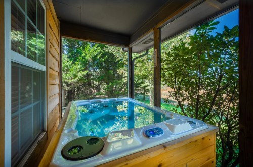 A hot tub on a porch surrounded by greenery and trees, offering a serene outdoor view.