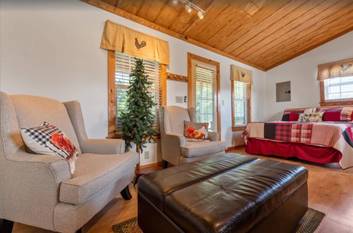 Cozy room with two armchairs, a coffee table, and a bed with plaid bedding, featuring wooden accents and natural light.