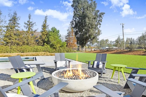 A cozy outdoor seating area with a fire pit surrounded by chairs and green tables, set against a scenic backdrop.