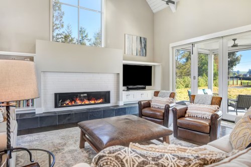 Bright living room with a modern fireplace, large windows, and comfortable seating, overlooking a scenic outdoor view.