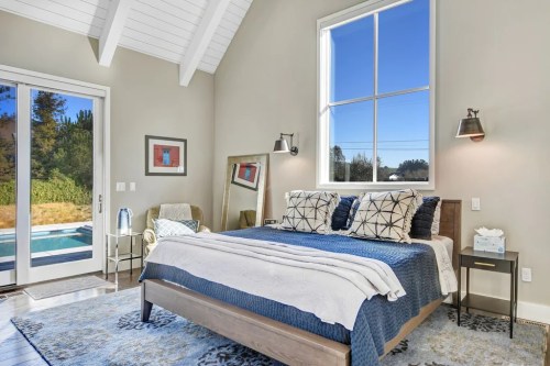 Bright bedroom with a large window, a cozy bed, and a view of the outdoors, featuring modern decor and natural light.