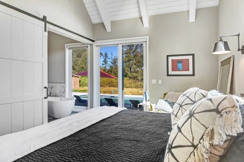 Cozy bedroom with a large bed, sliding door to a pool area, and modern decor featuring a bathtub and artwork.