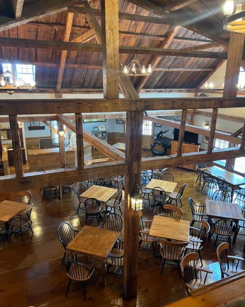 A spacious wooden interior with high ceilings, featuring tables and chairs arranged for dining.