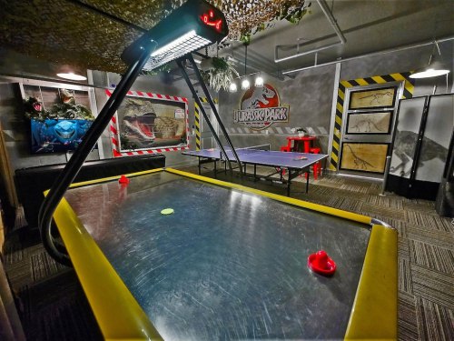 A game room featuring air hockey, a ping pong table, and Jurassic Park-themed decor on the walls.