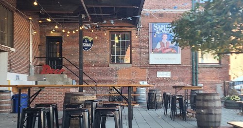 Outdoor seating area of a brick building with string lights, barrels, and a sign for Sam Adams Brewery.