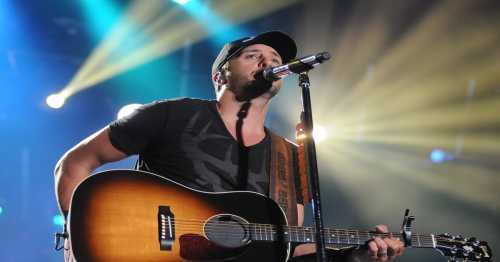 A musician performs on stage with an acoustic guitar, illuminated by colorful stage lights.