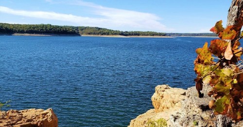 A serene lake surrounded by trees and rocky shores under a clear blue sky.