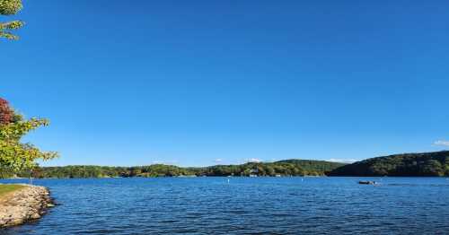 A serene lake surrounded by green hills under a clear blue sky, with a small boat on the water.