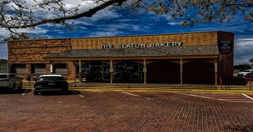 A brick building with a sign reading "The Slaton Bakery," featuring a yellow awning and parked cars in front.